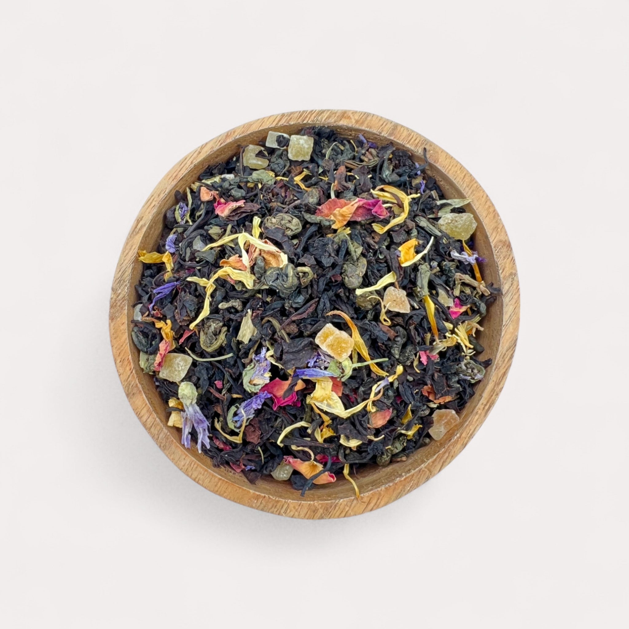Wooden bowl filled with colorful dried tea leaves on a light background - Strawberry Cream Black & Green Tea with Tropical Fruits