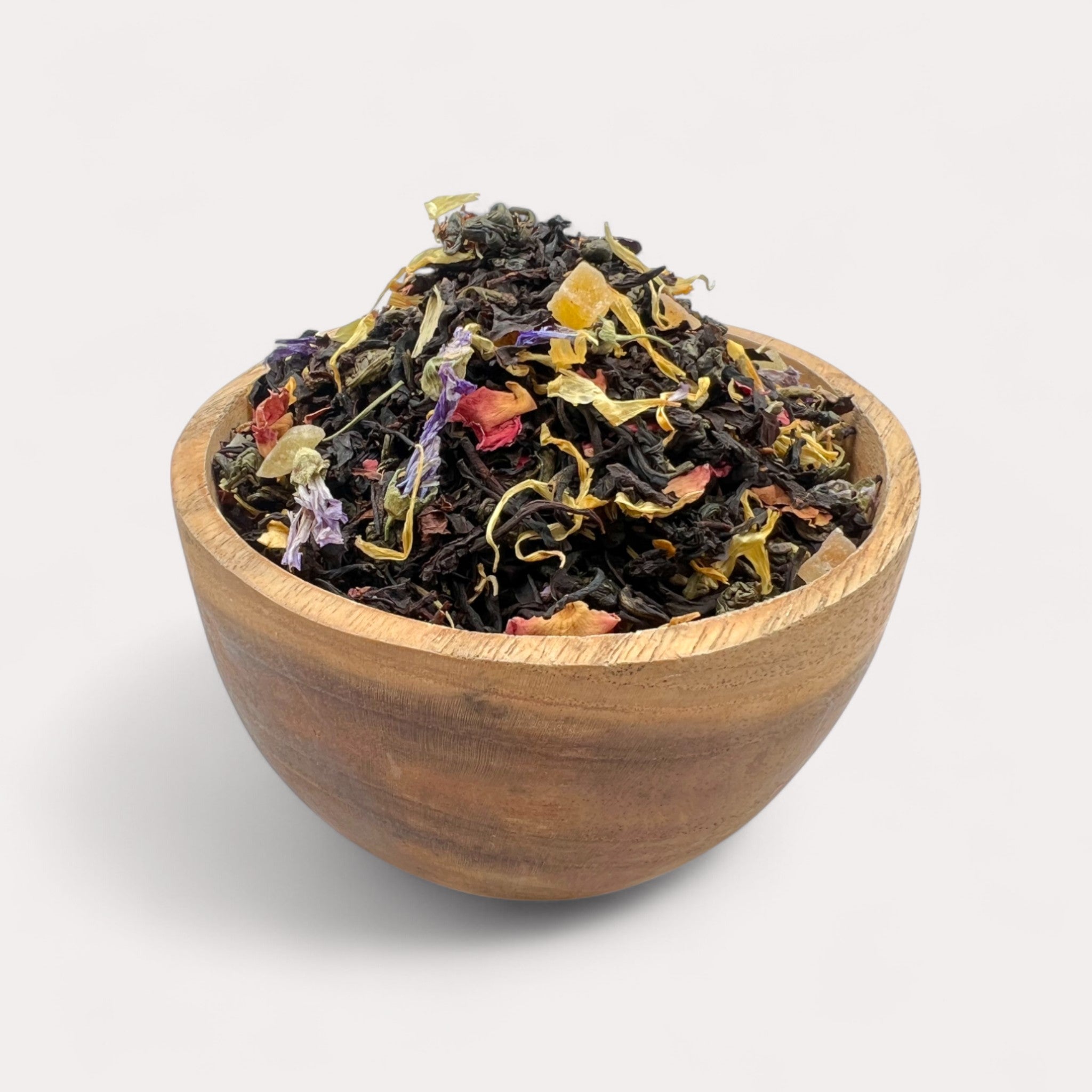 Wooden bowl filled with colorful dried tea leaves on a light background - Strawberry Cream Black & Green Tea with Tropical Fruits