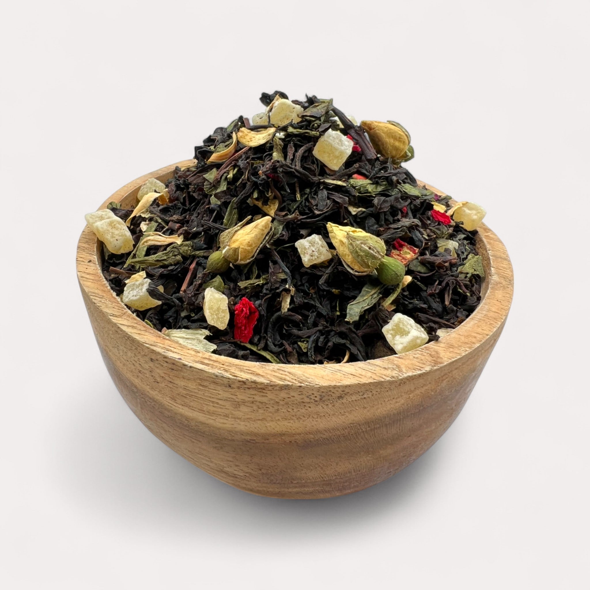 Wooden bowl filled with a mix of black and green tea leaves on a white background - Tropical Black & Green Tea with Pineapple, Soursop; Rose Petals – Garden in Bloom