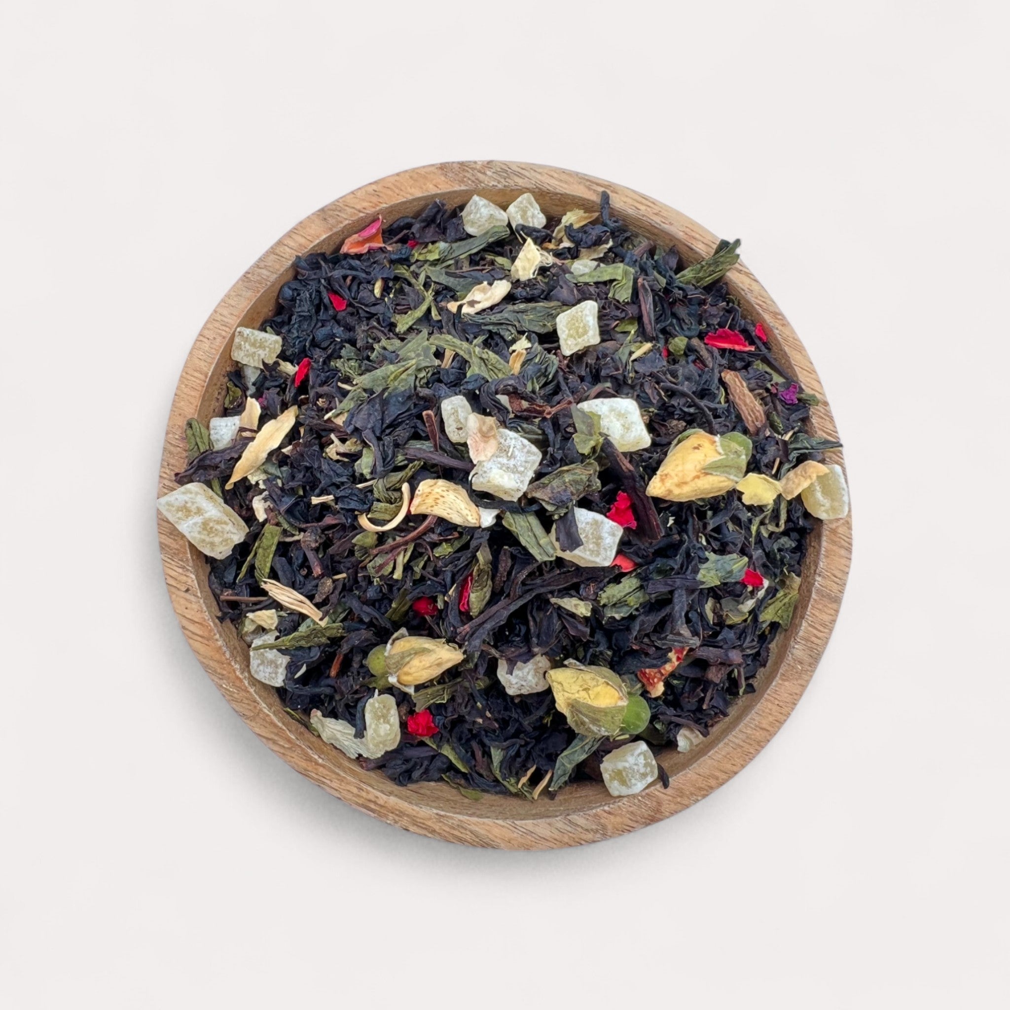 Wooden bowl filled with a mix of black and green tea leaves on a white background - Tropical Black & Green Tea with Pineapple, Soursop; Rose Petals – Garden in Bloom