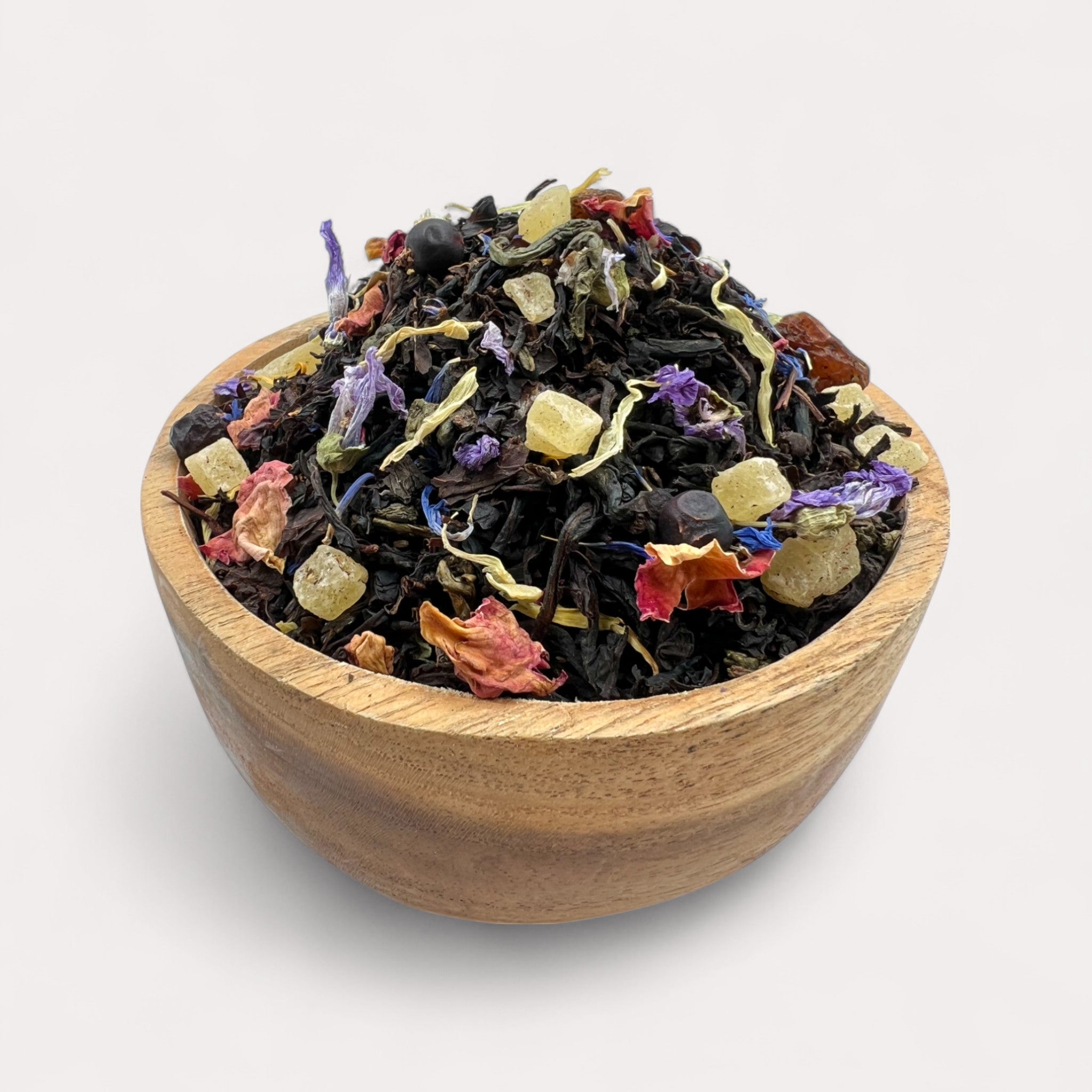 Colorful dried tea leaves in a wooden bowl on a light background - Exotic Black & Green Tea with Pineapple, Grape & Rose Petals
