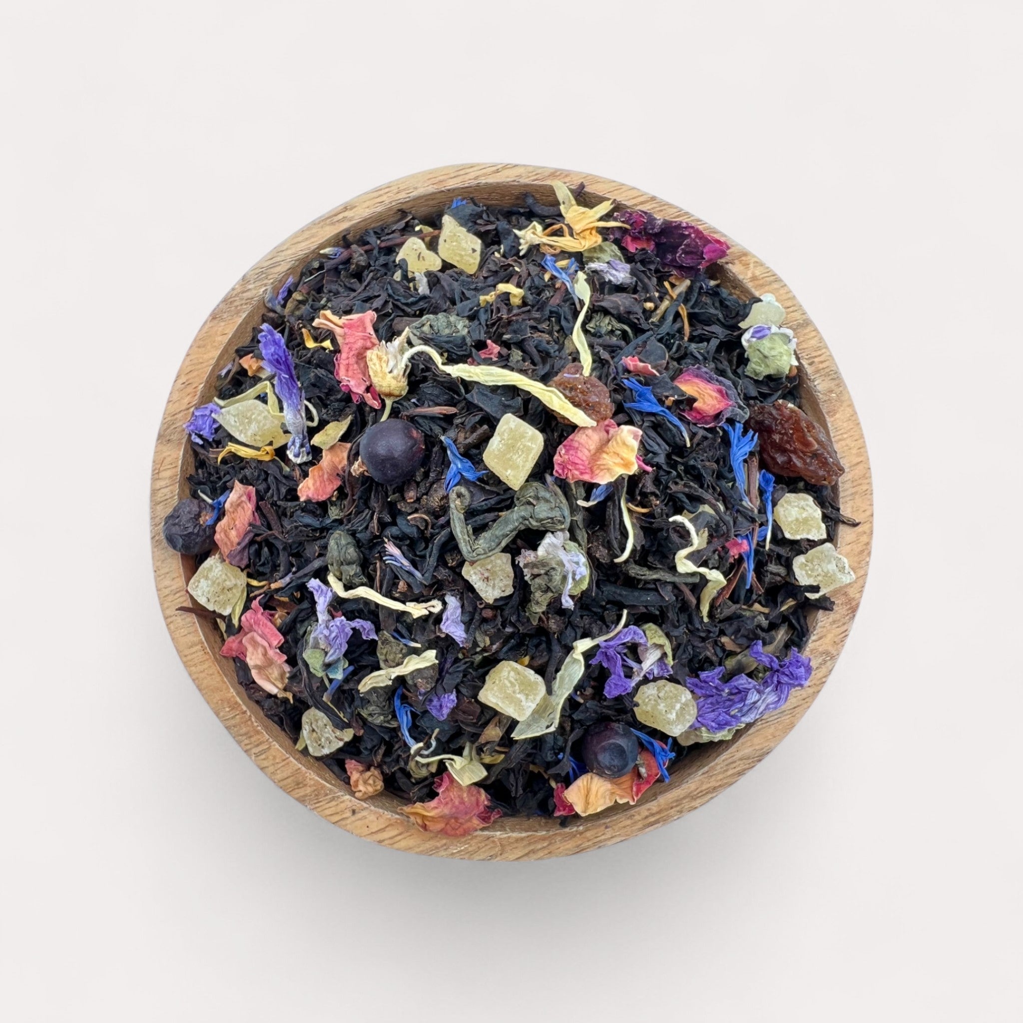 Colorful dried tea leaves in a wooden bowl on a light background - Exotic Black & Green Tea with Pineapple, Grape & Rose Petals