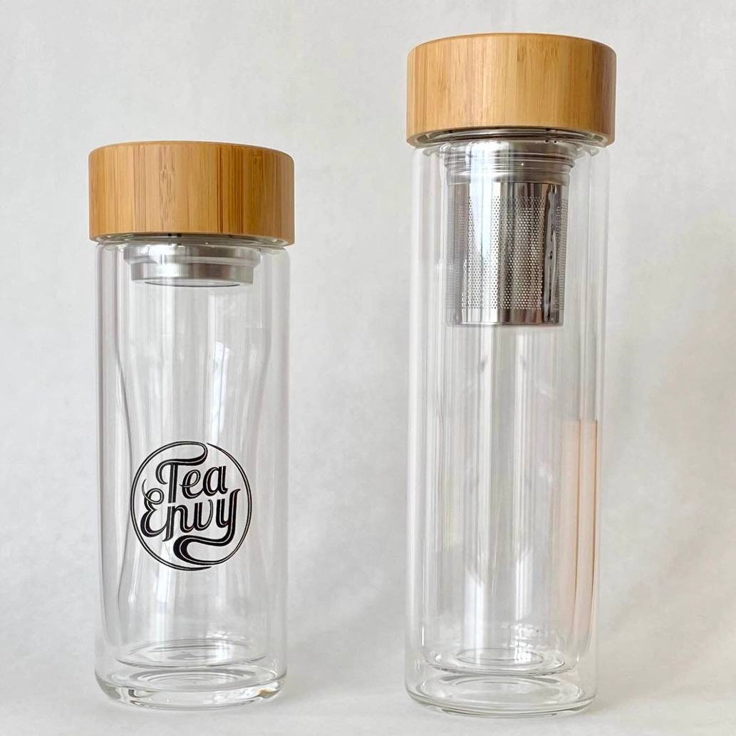 Two clear glass tea infusers with wooden lids on a white background