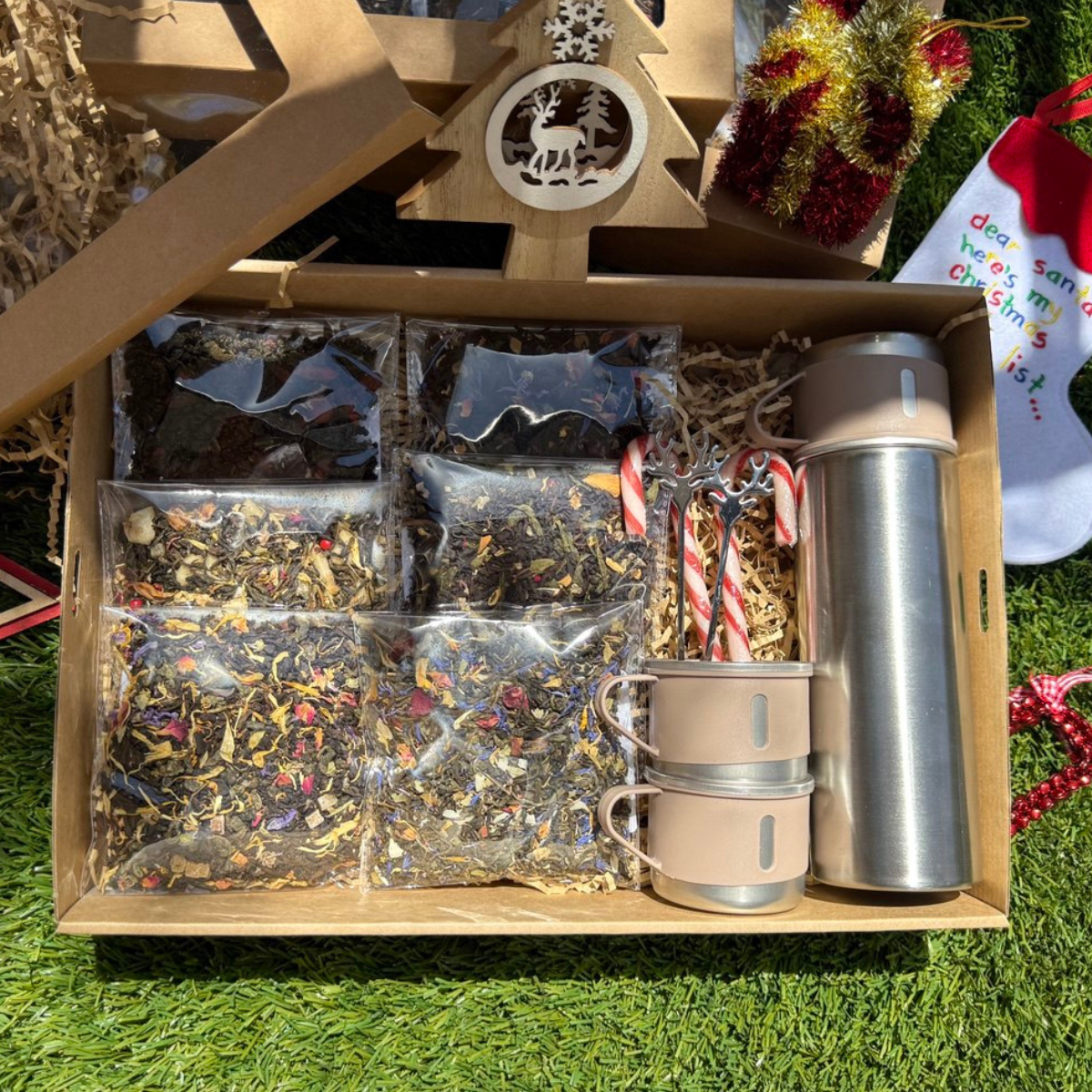 Tea gift set with tea bags, cups, and a thermos in a box on grass.